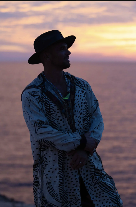Spooky in profile at dusk, with folded arms against the ocean and sunset.