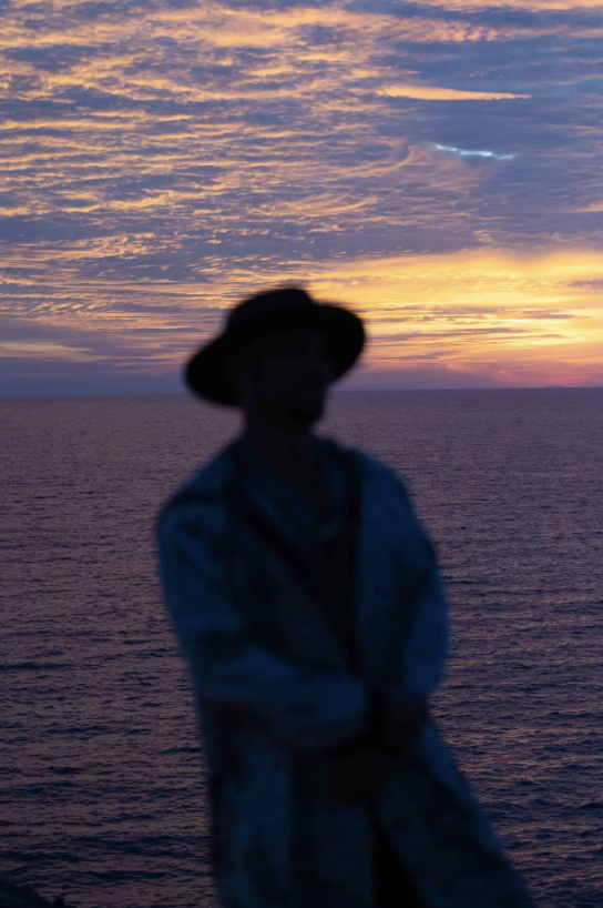 A soft-focus silhouette of Spooky against violet clouds and an ocean sunset.